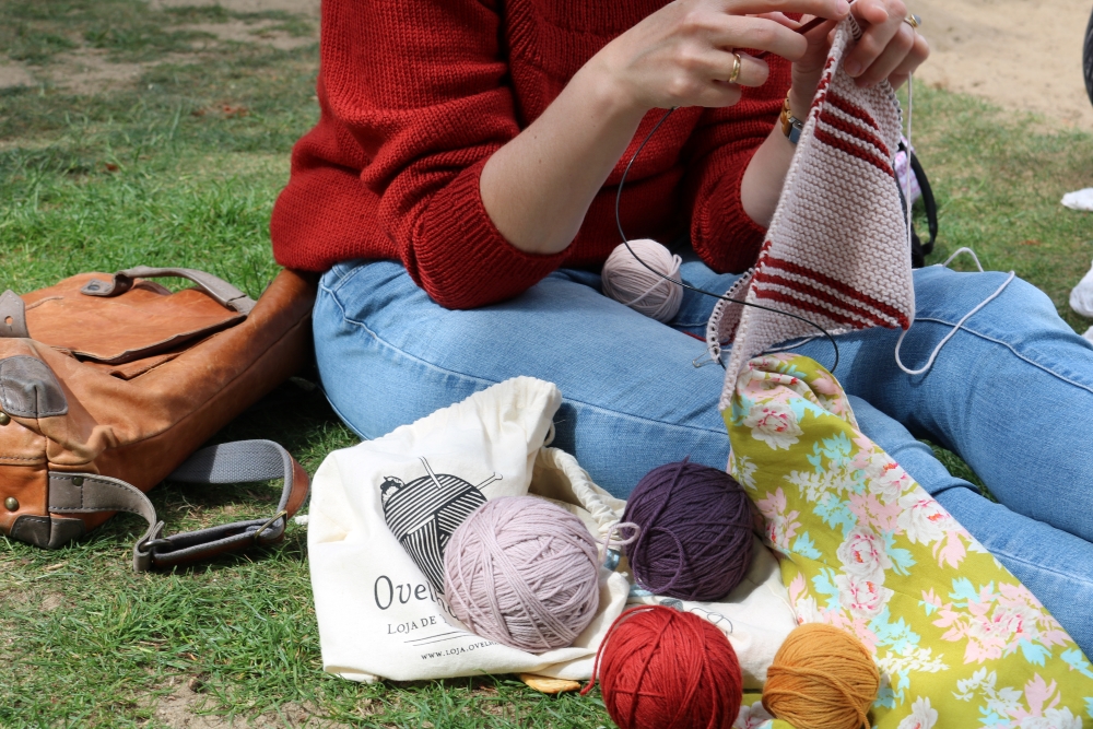 Different-coloured balls of yarn on a picnic blanket, legs and arms of a woman knitting